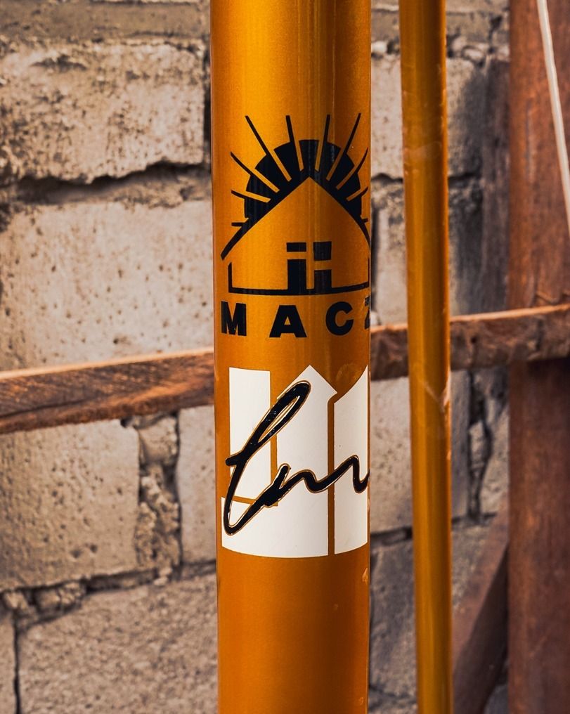 A gold groundbreaking pole wrapped in ribbon, marked with the MACZ house logo