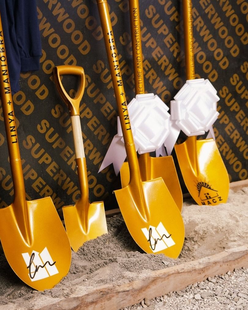 Gold ceremonial shovels with the MACZ mark, set in sand at the Francisco Residence groundbreaking