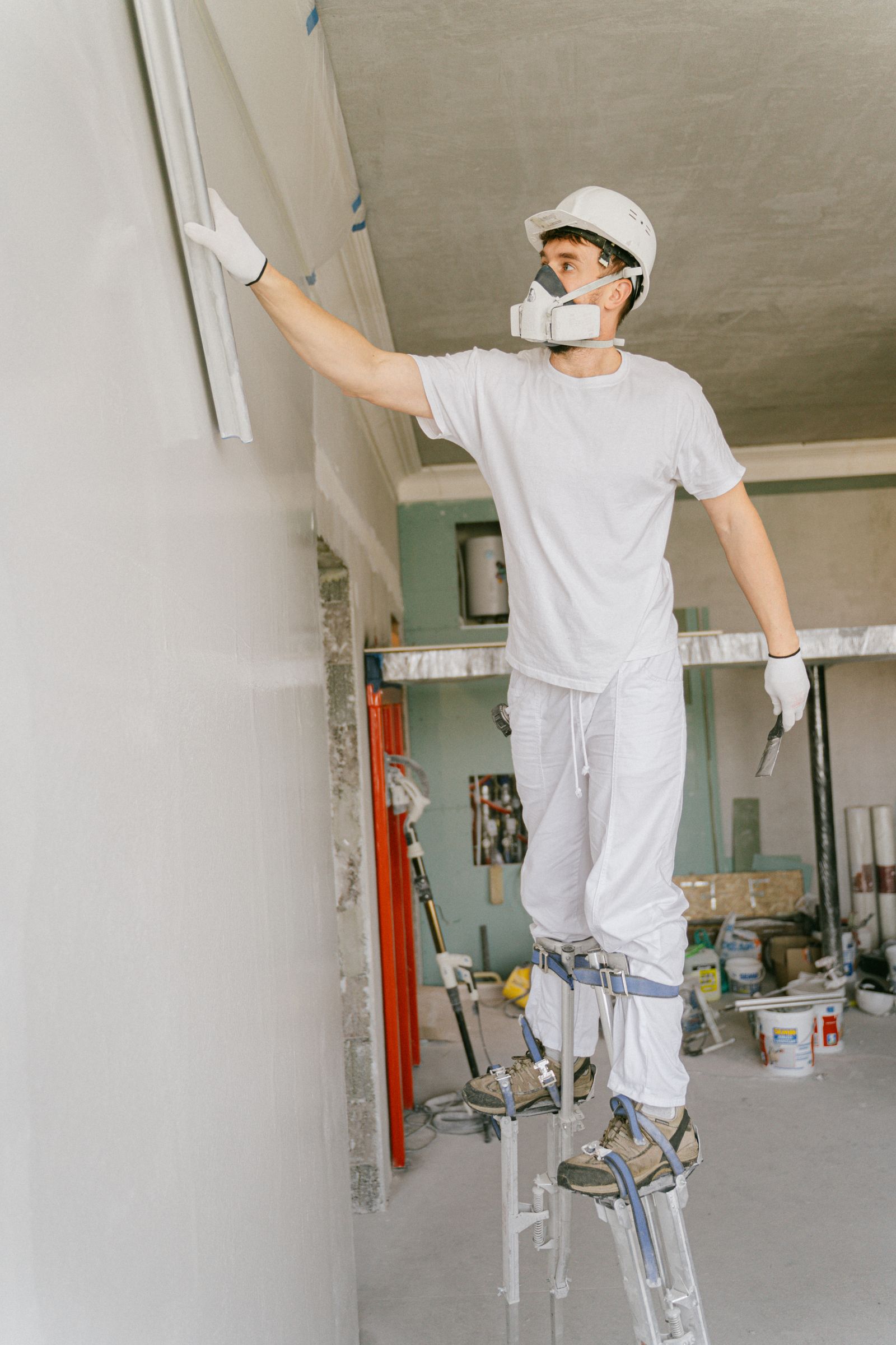 A plasterer on stilts finishing a wall during an interior fit-out