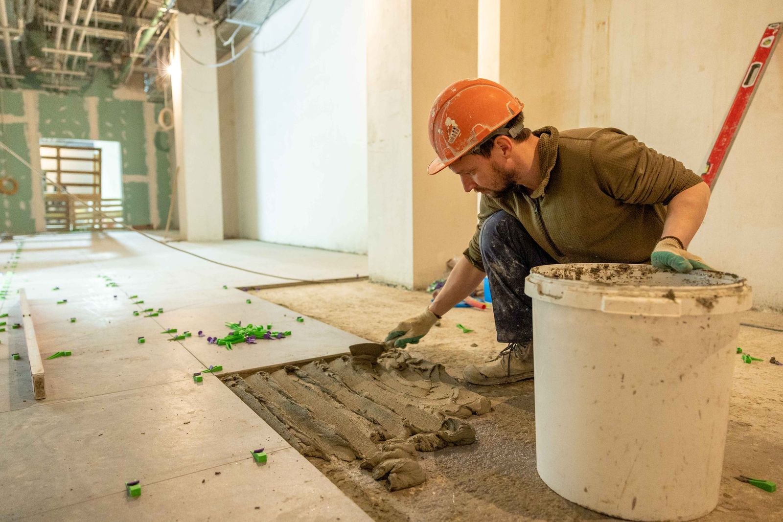 A tiler in a hard hat spreading adhesive on a floor during an interior renovation